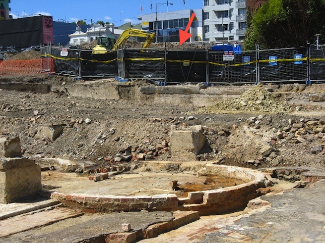 Archaeological dig at CUB site, with hoarding and mound in distance